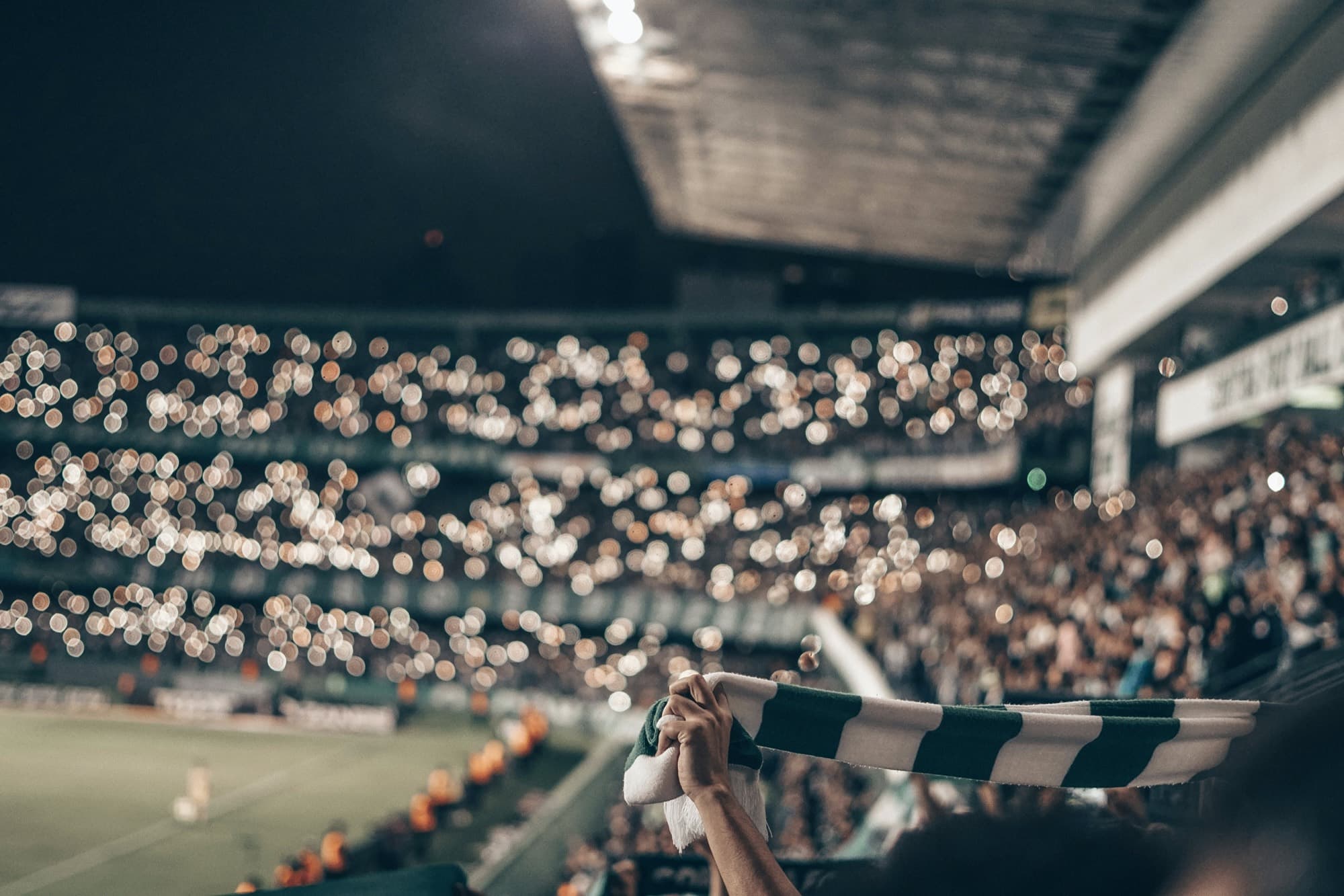 Supporters holding up a scarf in a floodlit stand on matchday